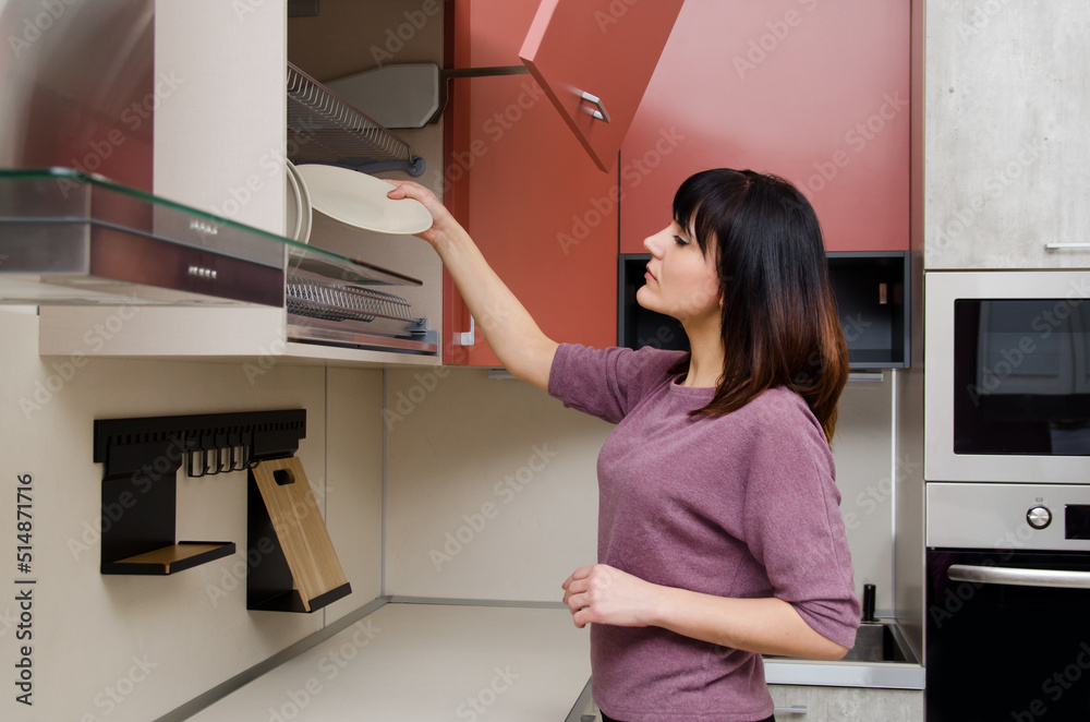 A young woman puts a plate in the dish drying rack in the kitchen. A young woman puts a plate in the dish drying rack in the kitchen.