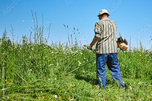A man mows the grass in the field with a trimmer. Yard care concept. Front view.
