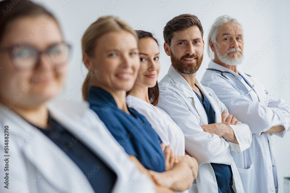 Group of doctors standing in a line keeping arms crossed and looking camera at the modern clinic Group of doctors standing in a line keeping arms crossed and looking camera at the modern clinic