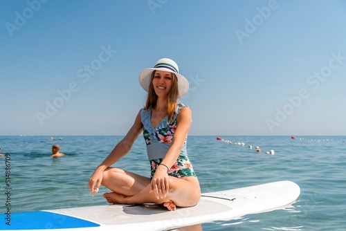 Happy young woman in swimsuit doing yoga on sup board in calm sea, early morning. Balanced pose - concept of healthy life and natural balance between body and mental development.