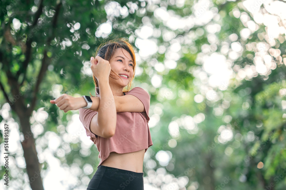 © oatawa - Fitness woman doing stretch exercise stretching her arms, female stretching for warming up before running or working out in the park outdoor.