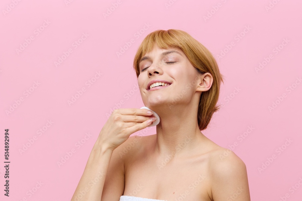 photo of a happy, sophisticated woman with blonde hair gathered back, standing on a pink background, wiping her face with a cotton pad and smiling pleasantly with her eyes closed with pleasure photo of a happy, sophisticated woman with blonde hair gathered back, standing on a pink background, wiping her face with a cotton pad and smiling pleasantly with her eyes closed with pleasure