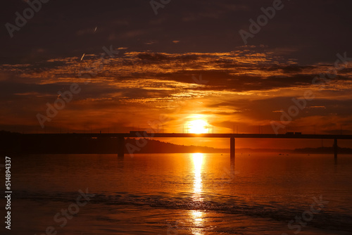 Beautiful red orange sunset over the surface of the river and the bridge. Summer nature landscape