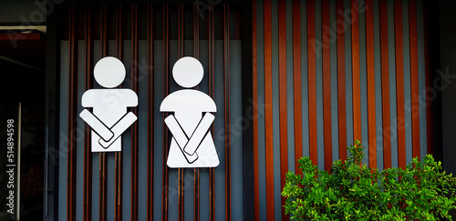 Public toilet sign or symbol of man and woman on wooden and gray or grey wall background with copy space. Entrance of restroom or lavatory with tree in front of room.  