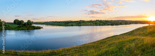 Summer panoramic rural landscape with green hills and blue calm river.Beautiful clouds in colorful sunrise sky over the land.