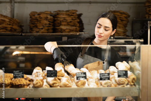 Cafe waitress girl puts fresh pastries on the cafe showcase, bakery worker