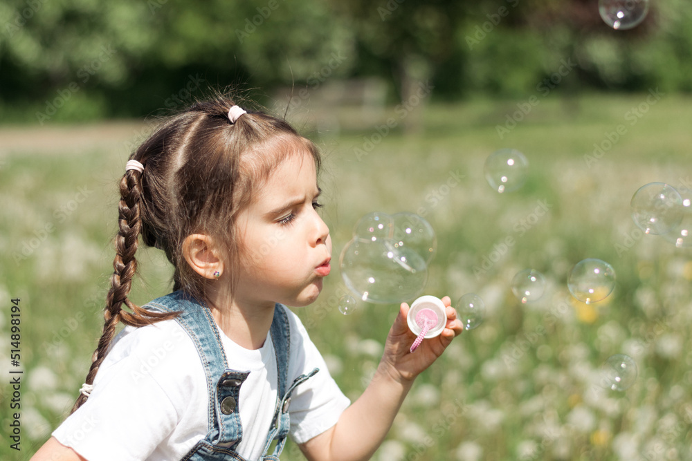 Portrait of a happy little caucasian girl blowing soap bubbles on a summer day in the park.Summer, childhood concept. Portrait of a happy little caucasian girl blowing soap bubbles on a summer day in the park.Summer, childhood concept.