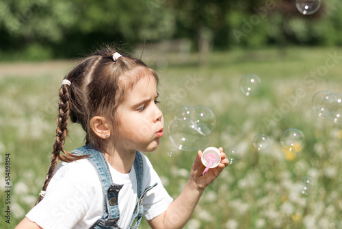 Portrait of a happy little caucasian girl blowing soap bubbles on a summer day in the park.Summer, childhood concept.