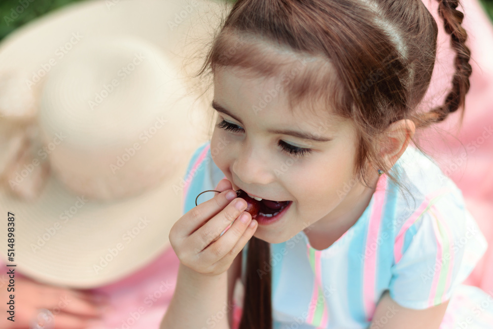 Close-up of cute little girl playing with cherry berries on a summer day in the park on a picnic.Summer, childhood concept. Close-up of cute little girl playing with cherry berries on a summer day in the park on a picnic.Summer, childhood concept.