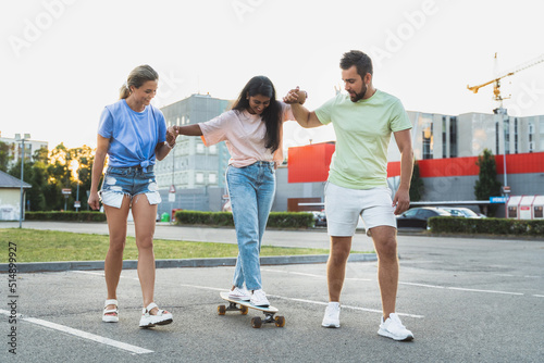 Diverse carefree friends having fun and riding longboard on parking lot