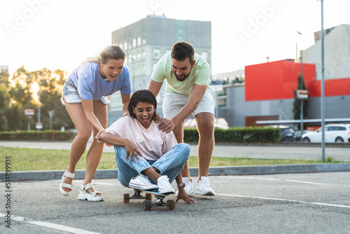 Diverse carefree friends having fun and riding longboard on parking lot