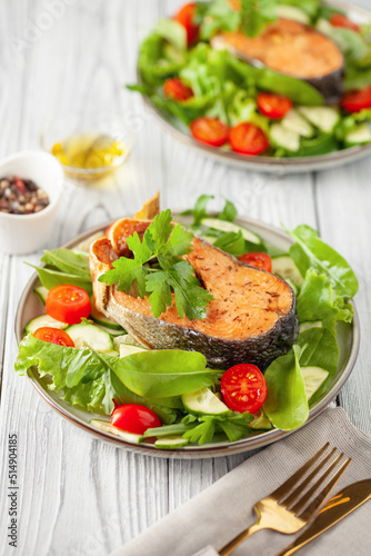 Fresh vegetable salad and baked salmon in a plate on the table. Mediterranean diet concept