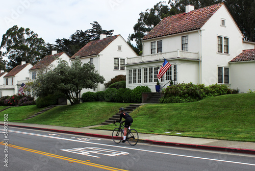 A classic American house with the flag of the United States. A cyclist on a special road for bicycles.