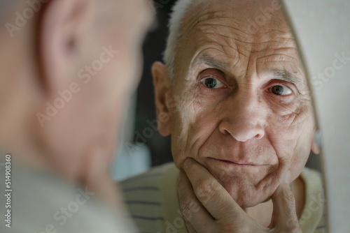 Senior man looking in mirror reflexion and touching wrinkled skin. Oldness and healthcare. photo