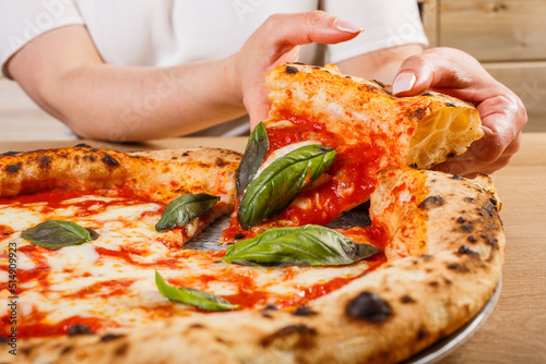 Fetta di pizza margherita napoletana con sugo di pomodoro, mozzarella basilico fresco tra le mani di una cliente photo