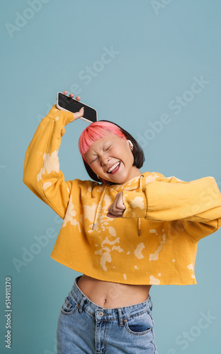 Asian girl in earphones dancing while listening music with cellphone