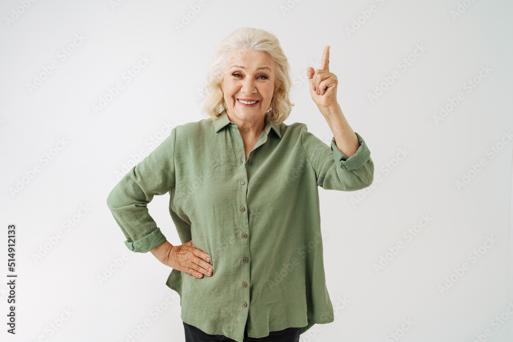 Grey senior woman in shirt smiling while pointing finger upward Grey senior woman in shirt smiling while pointing finger upward