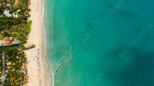 Aerial view of tropical sandy beach with fishing boats and a blue ocean. Trincomalee, Sri Lanka.