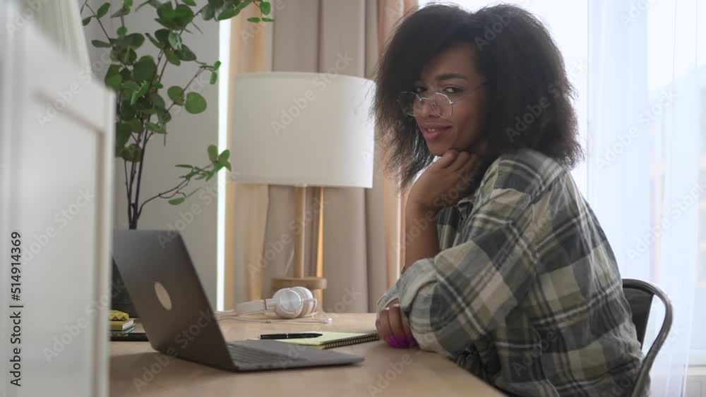 Young female student is writing in notebook and posing at table in modern apartment spbd. Portrait of beautiful american african female freelancer writes in diary and poses with smile for camera, sits