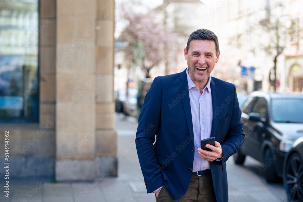 Businessman holding smart phone laughing on footpath Businessman holding smart phone laughing on footpath