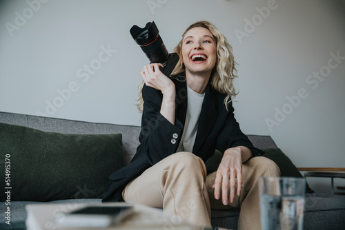 Happy photographer holding digital camera sitting on sofa photo