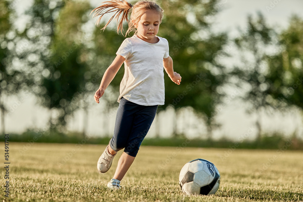 Blond girl playing soccer at sports field on sunny day Blond girl playing soccer at sports field on sunny day