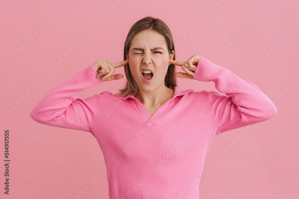 Young upset white woman wearing shirt frowning and plugging ears Young upset white woman wearing shirt frowning and plugging ears