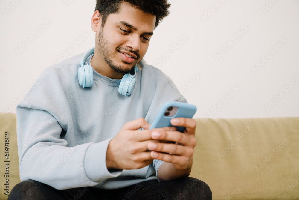 Young indian man with headphones on neck playing mobile games Young indian man with headphones on neck playing mobile games