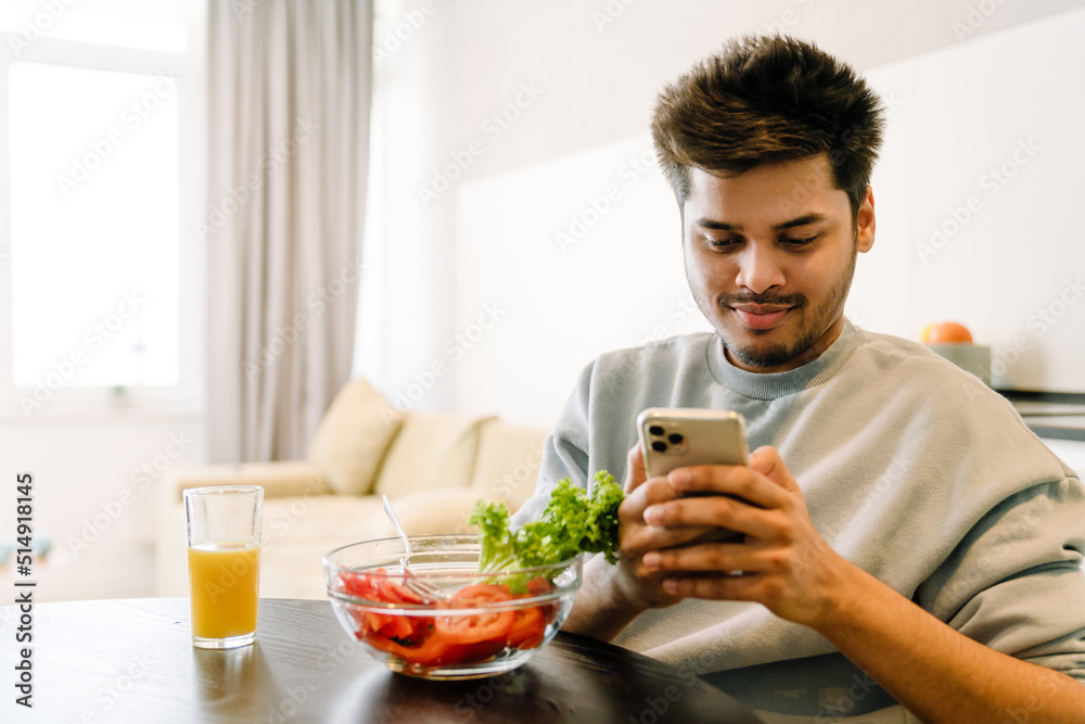Young indian smiling man looking on phone while having lunch Young indian smiling man looking on phone while having lunch