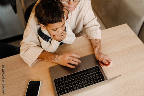 Young african mother working with laptop holding her son close-up