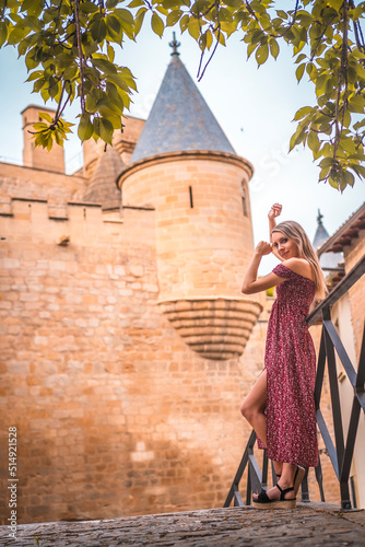 Portrait of a blonde woman next to a medieval castle in a red dress