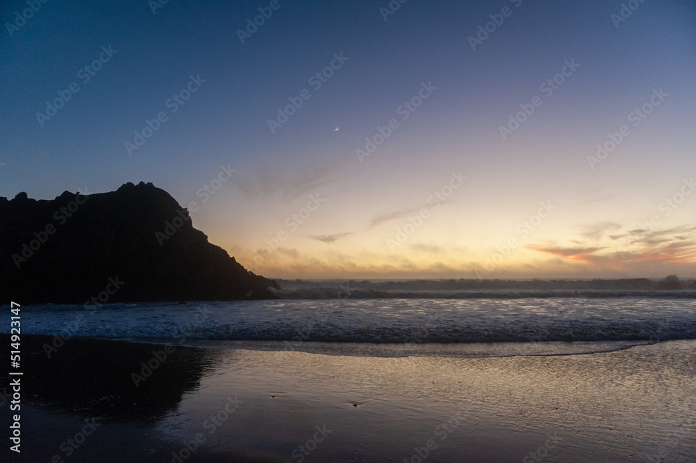 Rocks in the surf of Pfeiffer beach, around sunset. Deep yellow orange clouds color the sky.