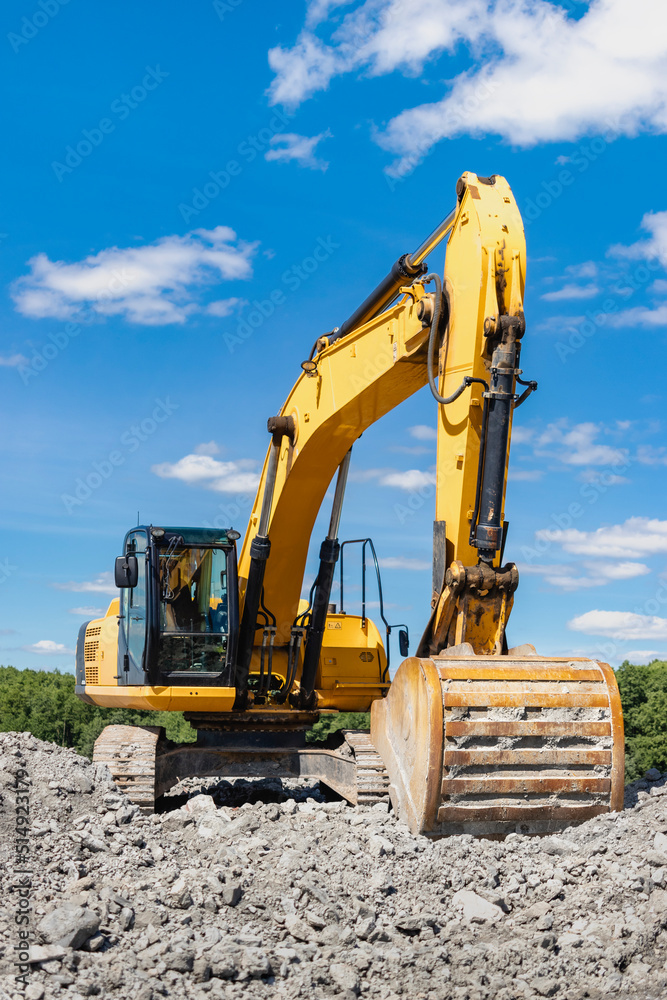 Powerful industrial excavator in a quarry against a blue cloudy sky. Loading crushed stone and soil with an excavator. Earth-moving equipment and earthworks. Powerful industrial excavator in a quarry against a blue cloudy sky. Loading crushed stone and soil with an excavator. Earth-moving equipment and earthworks.