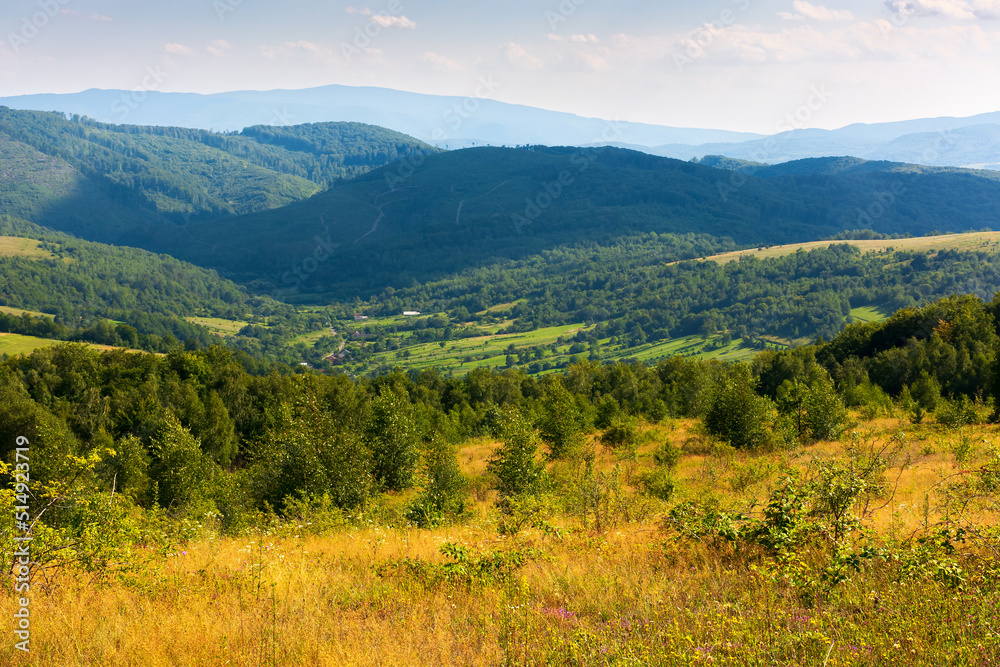 mountain scenery on an idyllic summer day. countryside landscape of capathian alps with fresh green meadows an forested hills. village in the distant valley. clouds on the blue sky in afternoon light