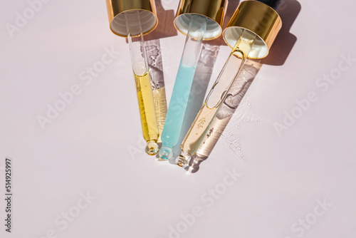 Close up of pipettes with pouring liquid essential oil or serom on pink background. Dropper with a falling drop of aromatherapy oil close-up photo