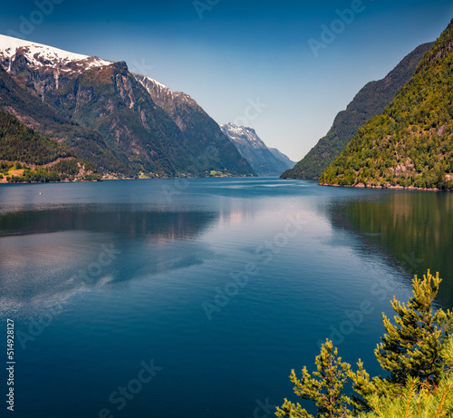 Sunny summer scene of Hardangerfjord fjord, Lofthus village location, Norway, Europe. Deep canyon with snow cap on mountain top. Traveling concept background. photo