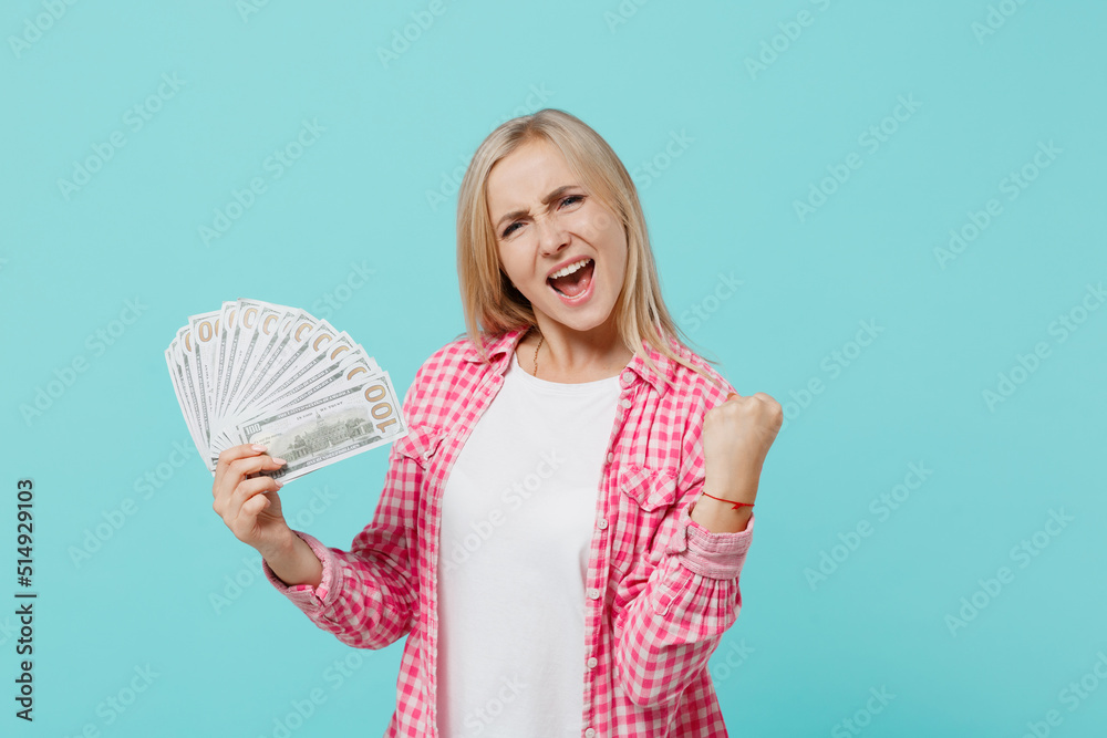 Young happy surprised woman she 30s in pink shirt white t-shirt holding fan of cash money in dollar banknotes do winner gesture isolated on plain pastel light blue background People lifestyle concept Young happy surprised woman she 30s in pink shirt white t-shirt holding fan of cash money in dollar banknotes do winner gesture isolated on plain pastel light blue background People lifestyle concept