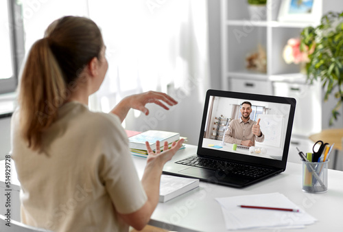 school  education and distance learning concept - female student with teacher on laptop computer screen having video call or online class at home and showing thumbs up