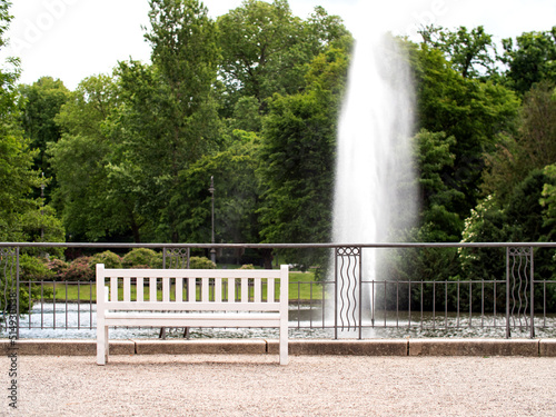 Empty white park bench. Fountain in in the background. Solitude and relax.