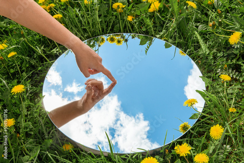 nature concept - hand touching sky reflection in round mirror on summer field photo