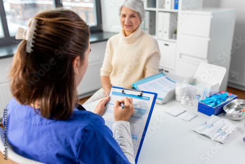 medicine, health and vaccination concept - doctor with clipboard and senior woman at hospital