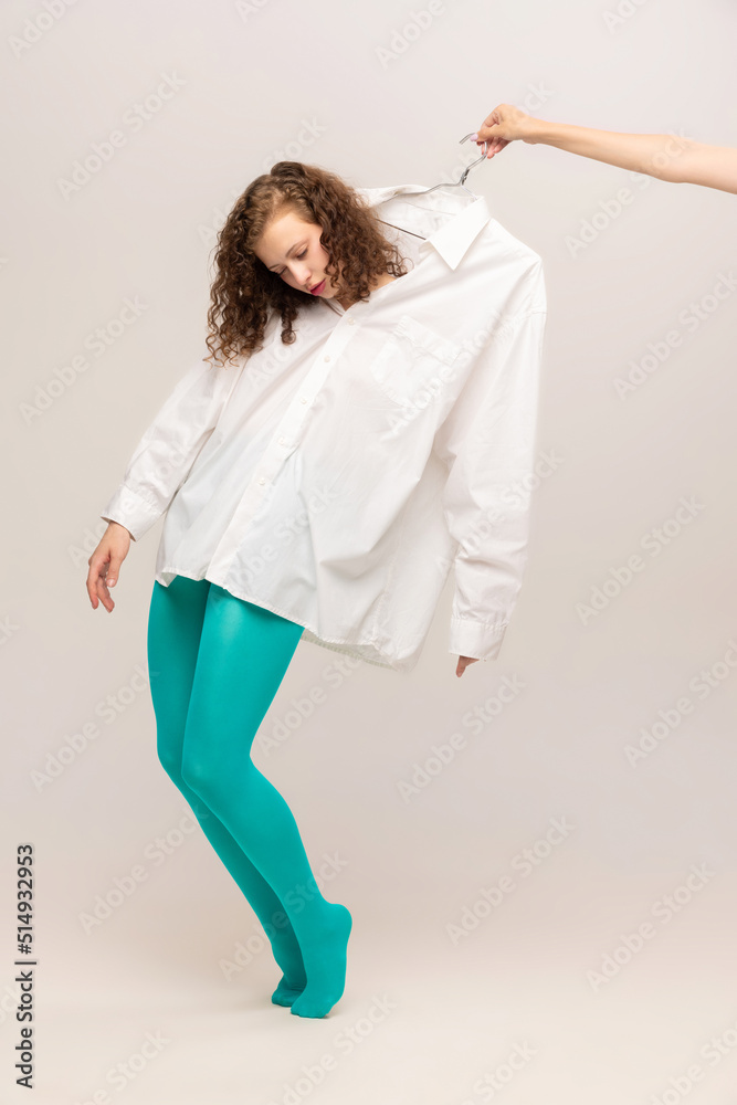 Young girl in white shirt and blue tights controlled by the other hand isolated over white background. Addiction, control, beauty, queer, freak, fashion concept. Young girl in white shirt and blue tights controlled by the other hand isolated over white background. Addiction, control, beauty, queer, freak, fashion concept.