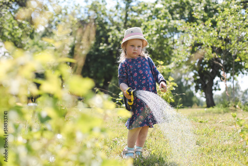 Adorable little girl playing with a garden hose on hot and sunny summer day