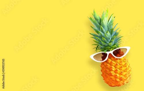 Summer background. Pineapple in sunglasses on yellow background.