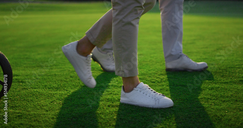 Two golfers legs walking on green grass field. Golf team carry sport equipment.