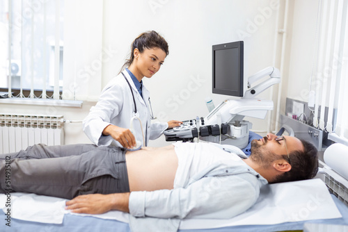 Ultrasound diagnostic of stomach on abdominal to man in clinic, closeup view. Doctor runs ultrasound sensor over patient's tummy and looks at image on screen. Diagnosis of internal organs.