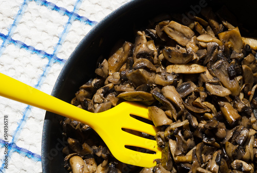 Champignon mushrooms fried, cooked in a frying pan with a yellow spatula, close-up. photo
