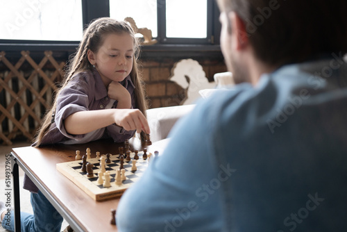 Father and daughter playing chess in the living room at home.