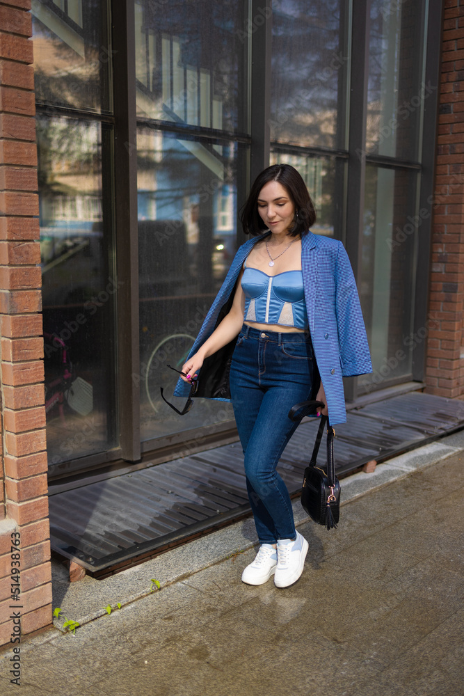 brunette girl in a blue jacket and jeans walks through the city streets