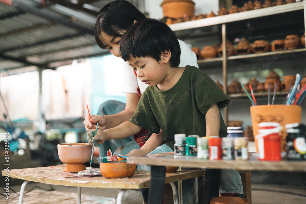 Fototapeta premium Happy family moment Mother teaching son how to painting mug cup ceramic workshop. Child creative activities and art. Kid playing pottery workshop. Developing children's learning skills.